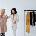 A fashion stylist helps a woman choose clothing in a stylish boutique setting.
